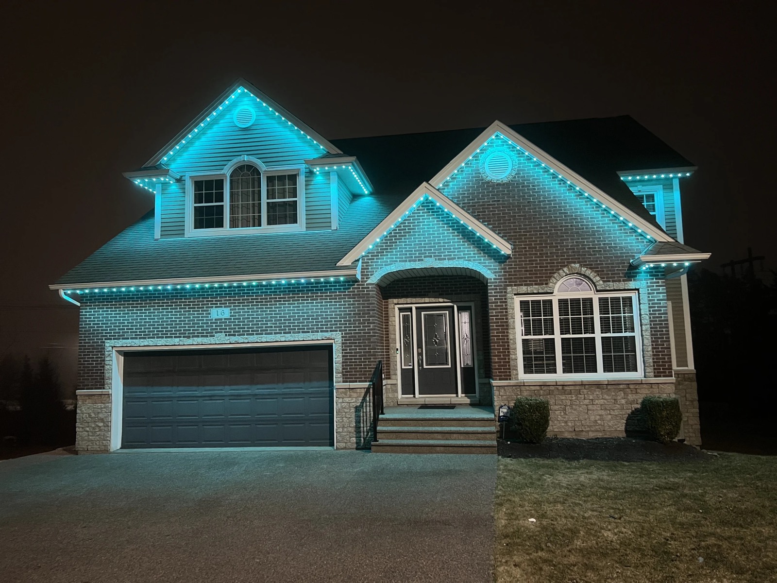 Two-storey brick home washed in teal from its roofline channel