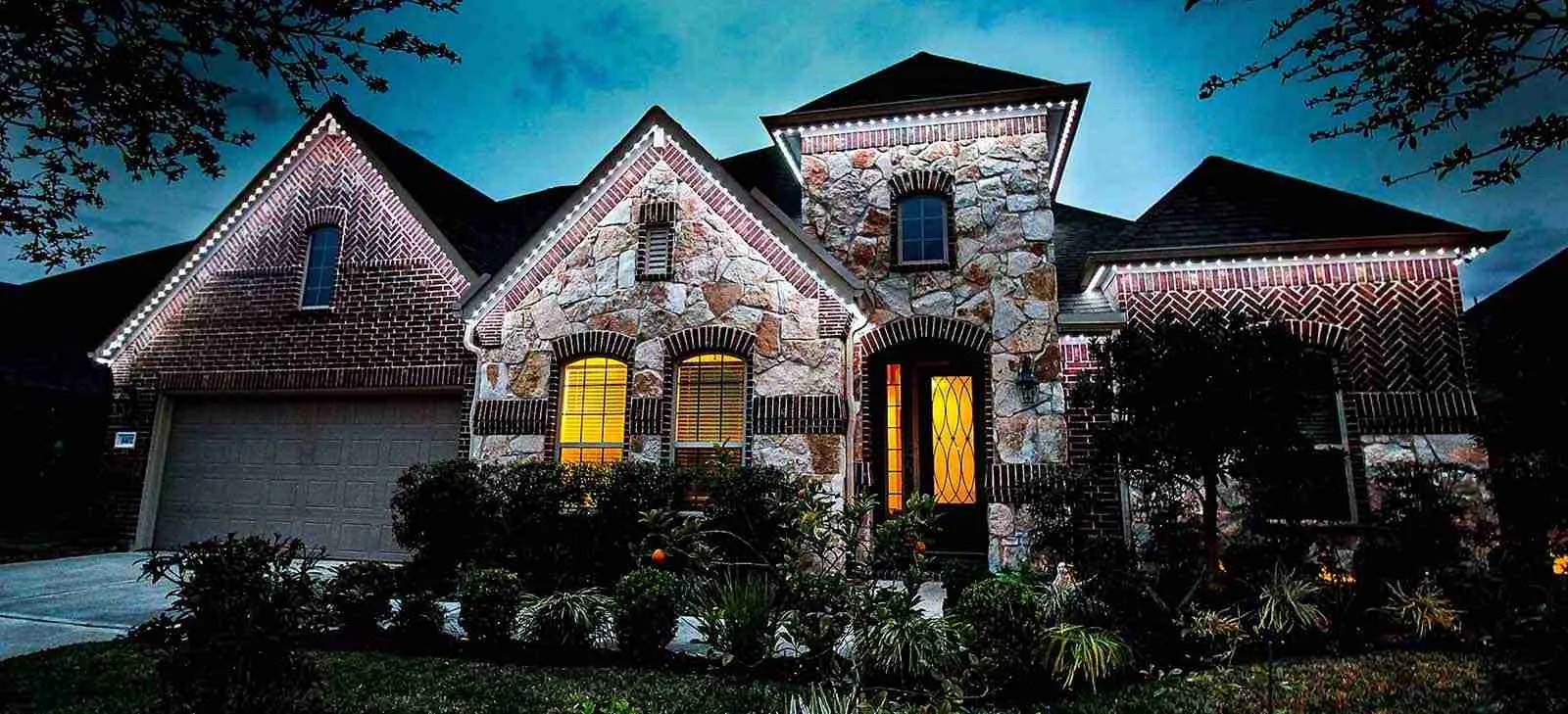 Stone and brick home lit warm white along the eaves and gables